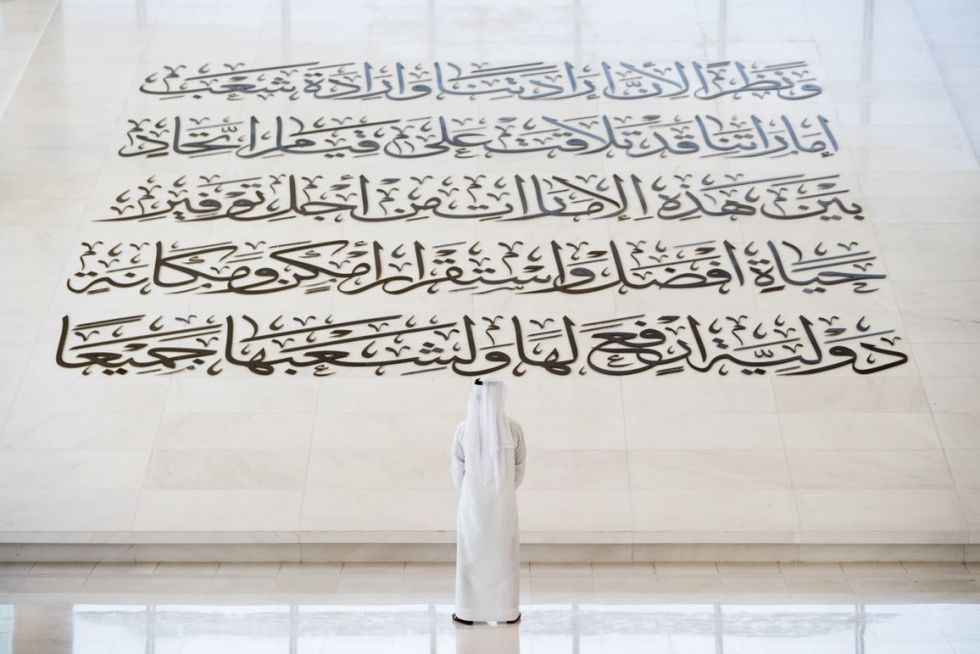 Man in white robe admires large Arabic calligraphy on a marble floor at Etihad Museum, Dubai, UAE