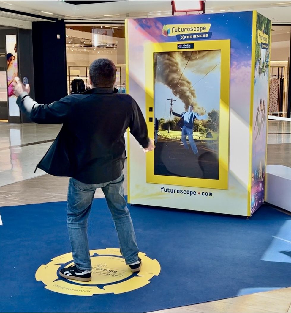 Man interacting with a virtual reality tornado simulation booth in a mall.