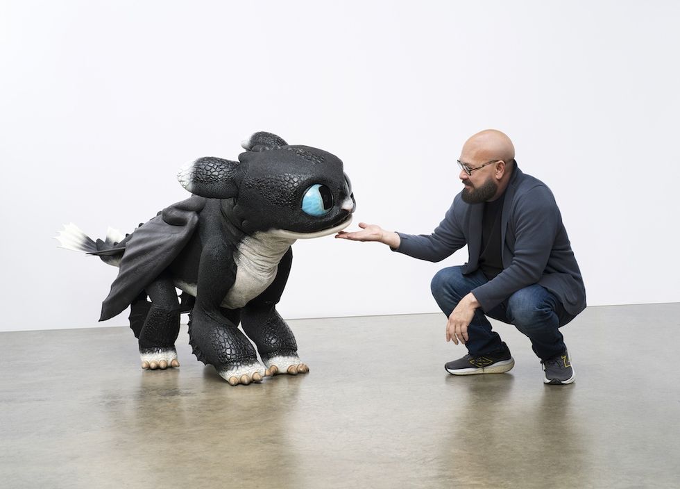 Man interacting with large, cute dragon-like creature in bright room.