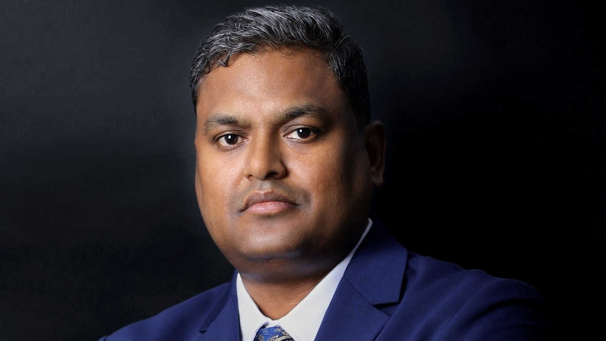 Man named Arun Thangaraj in a blue suit and tie with a dark background.