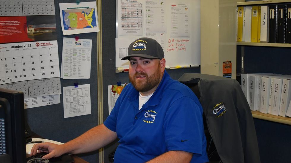 Man named Benjamin DeGarmo in blue Chance Rides uniform and cap working at a desk with a computer and office folders.