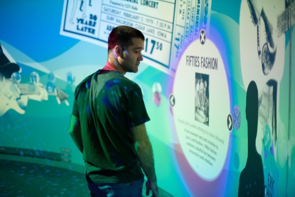 Man observing colorful, interactive museum exhibit about 1950s fashion and music history.