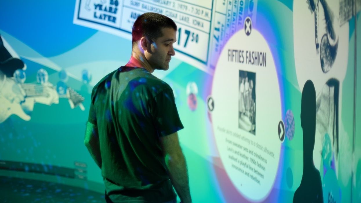 Man observing colorful projetion mapped wall display about fifties fashion and music history.