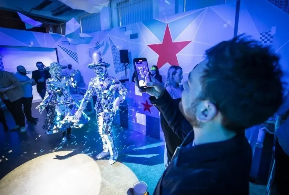 Man photographs people in reflective outfits at a blue-lit event.