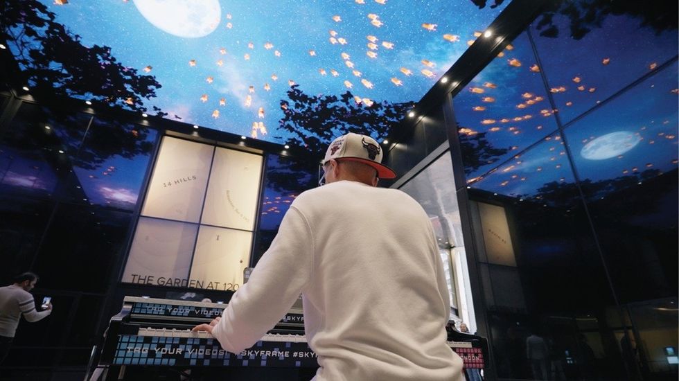 Man playing piano under a digital sky ceiling with moon and stars.