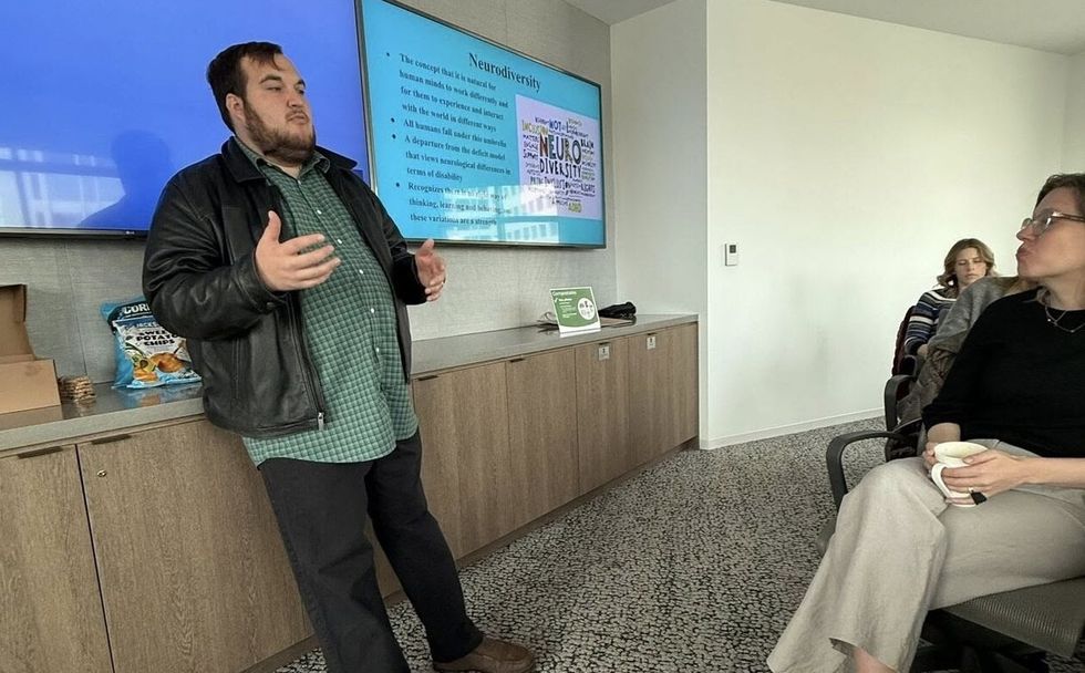Man presenting on neurodiversity to seated audience, with slides on screen.