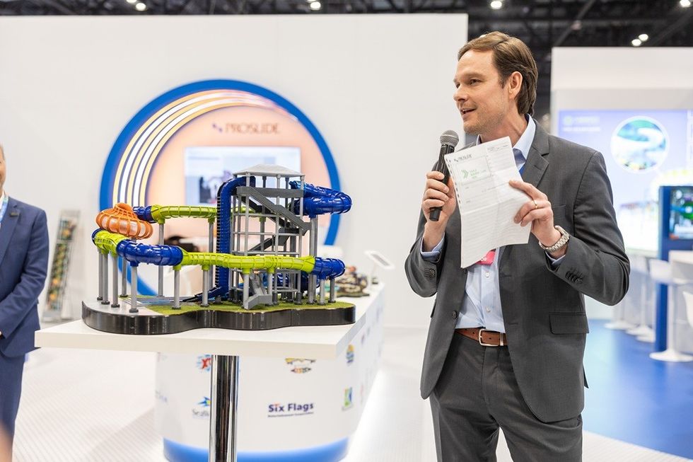Man presenting with a microphone next to a water slide model at an exhibition.