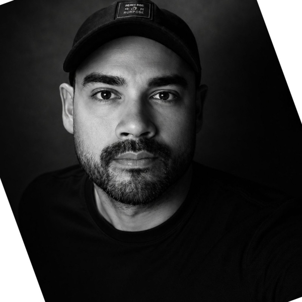 Man with a beard wearing a cap, captured in black and white portrait.