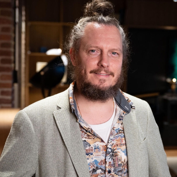 Man with a bun in a patterned shirt, standing in a stylish bar environment.