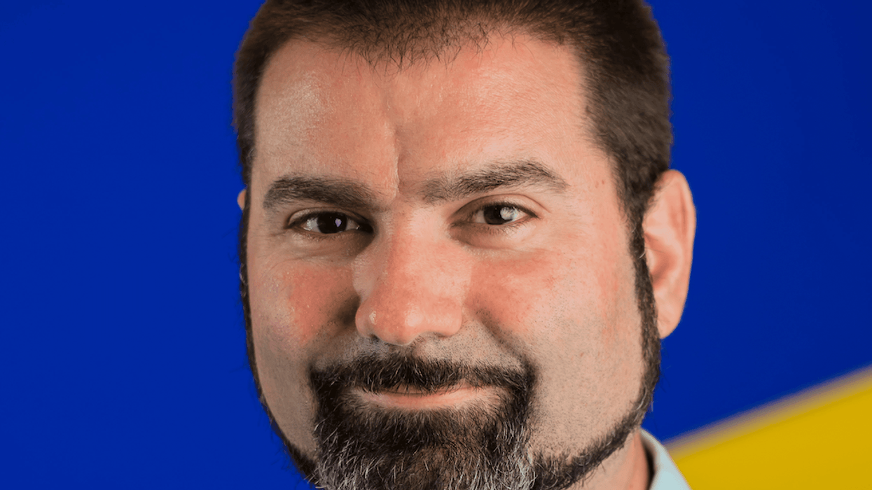 Man with beard smiling against blue and yellow background.