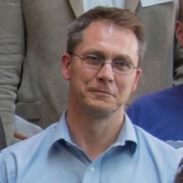 Man with glasses and blue shirt, standing against a blurred background.