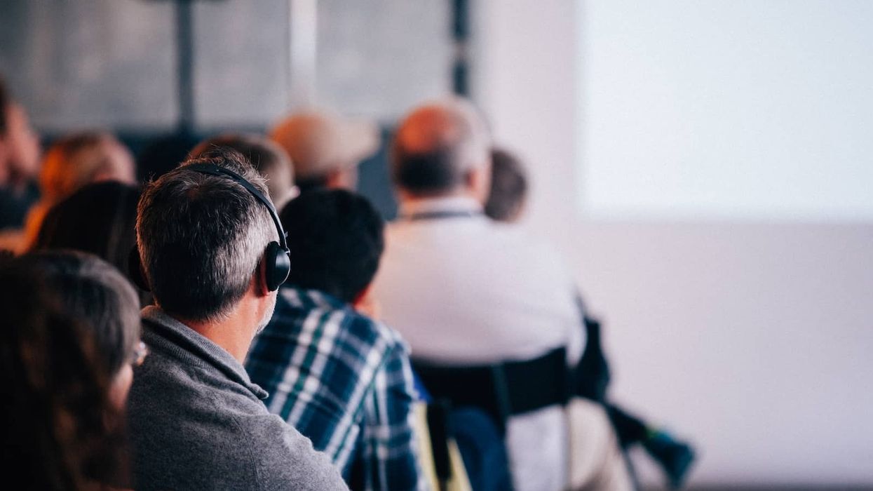 Man with headphones using earphone for reel time translation and Audience people sitting rear at the business seminar on the white screen in Conference Hall.