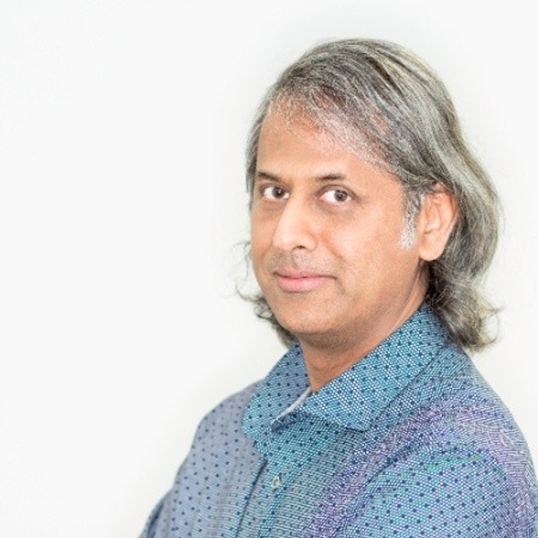 Man with long gray hair in a patterned blue shirt against a light background.