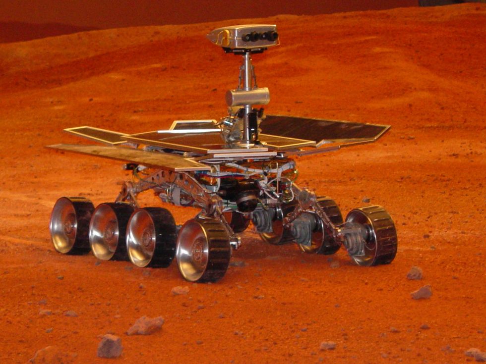 Mars rover on a red, rocky terrain with solar panels and six wheels.