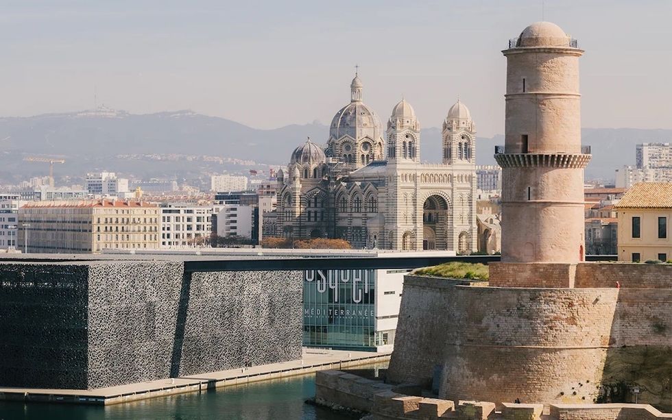 Marseille's MuCEM, lighthouse, and cathedral with mountains in the background.