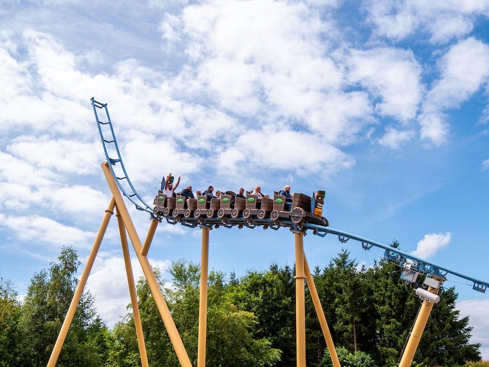Mauis Peak Roller coaster ascending with people waving hands, set against a cloudy sky.