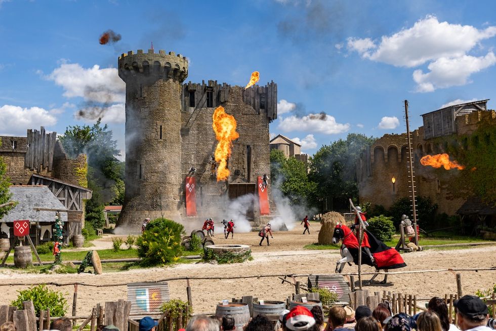 Medieval castle event with knights, fire effects, and spectators under a blue sky - \u200bLe Secret de la Lance show at Puy du Fou