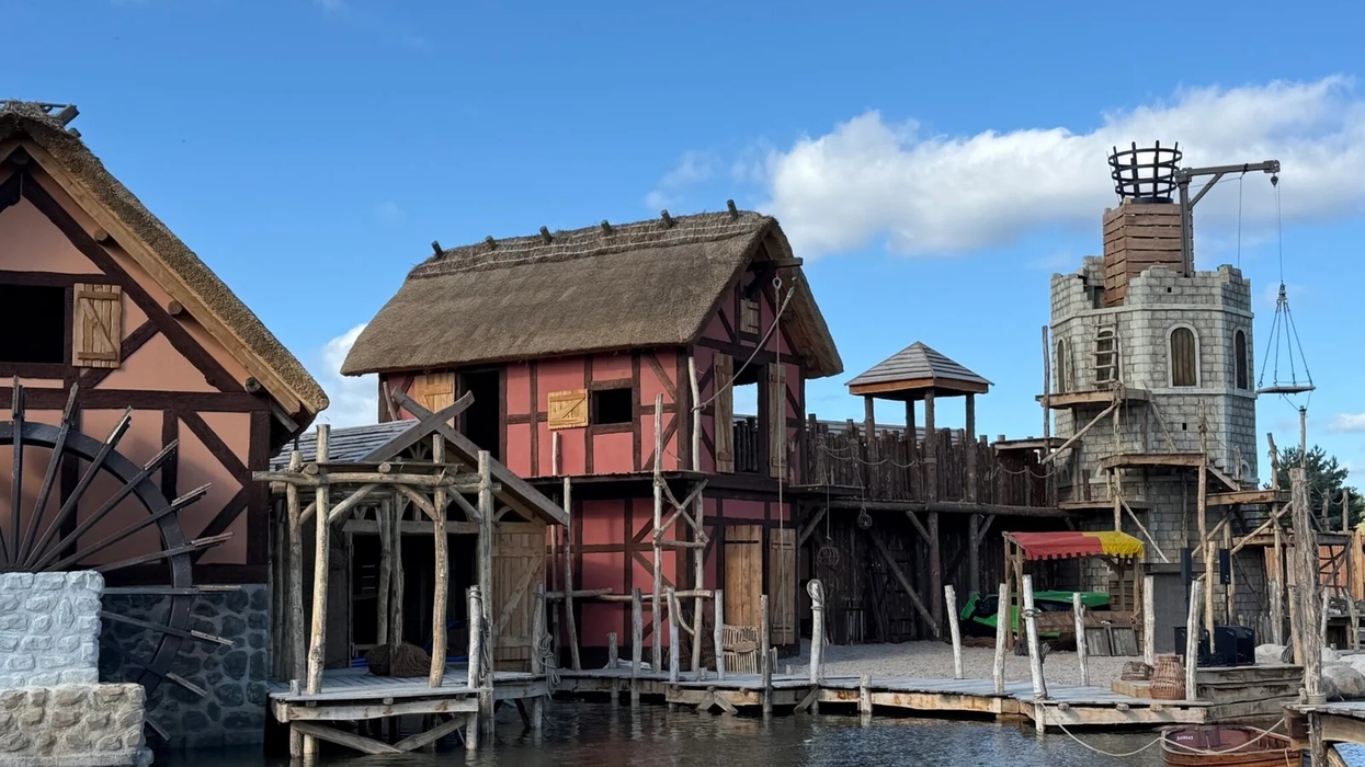 Medieval-style buildings by a river at Kynren, featuring a waterwheel and a stone tower.