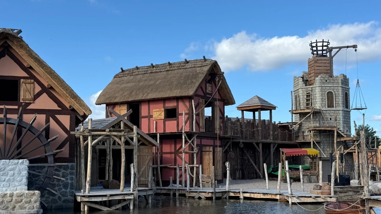 Medieval-style buildings by a river at Kynren, featuring a waterwheel and a stone tower.