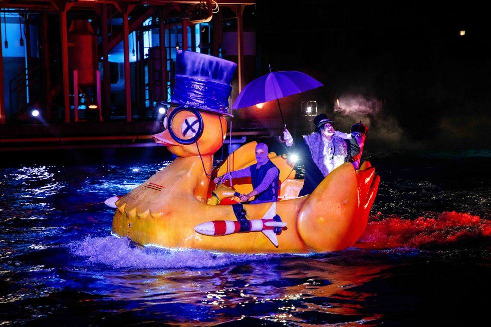 Men in costume on a giant duck float, illuminated at night on the water.