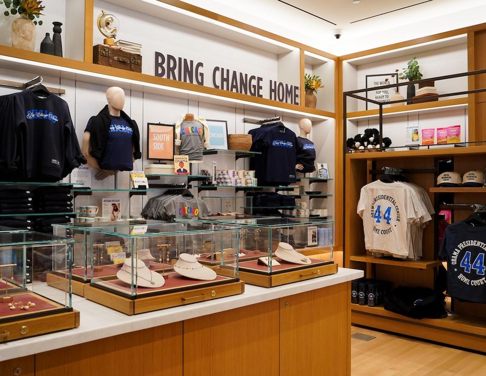 Merchandise display at Obama Presidential Center with shirts and jewelry under "Bring Change Home" sign.