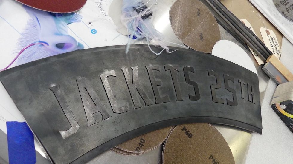 Metal plaque inscribed with "JACKETS 25TH" among various craft tools.