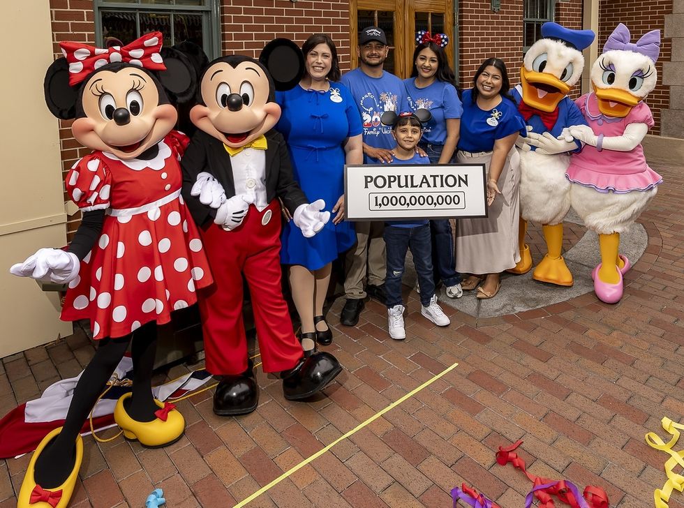 Mickey, Minnie, Donald, and Daisy with a family holding "Population 1,000,000,000" sign at Disneyland