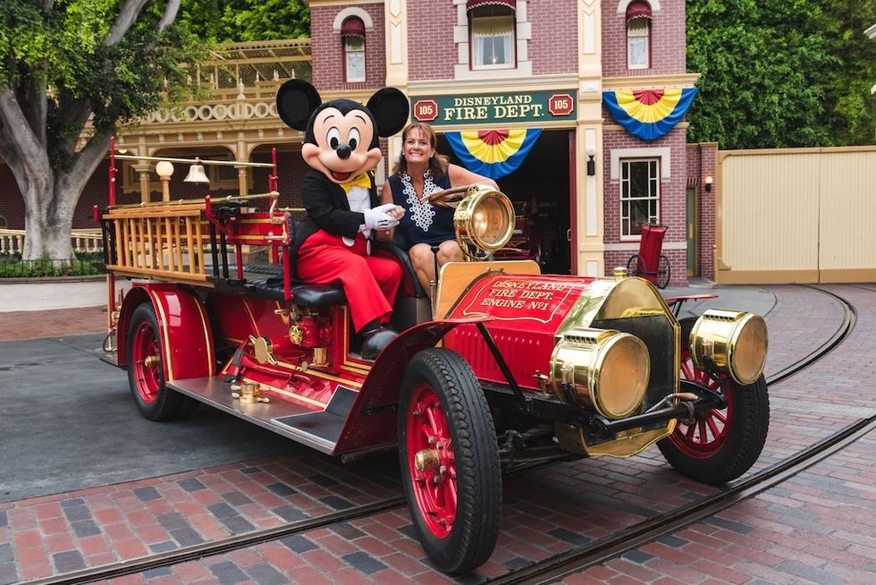 Mickey Mouse and a smiling woman sit on a vintage fire truck at Disneyland Fire Dept.