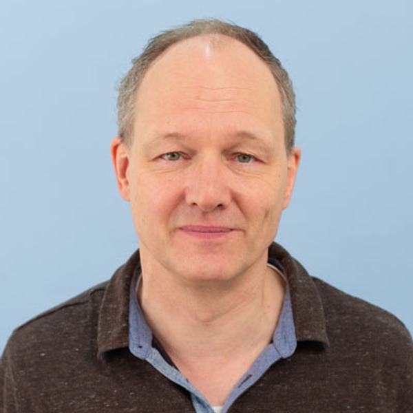Middle-aged man with short hair smiling against a blue background.