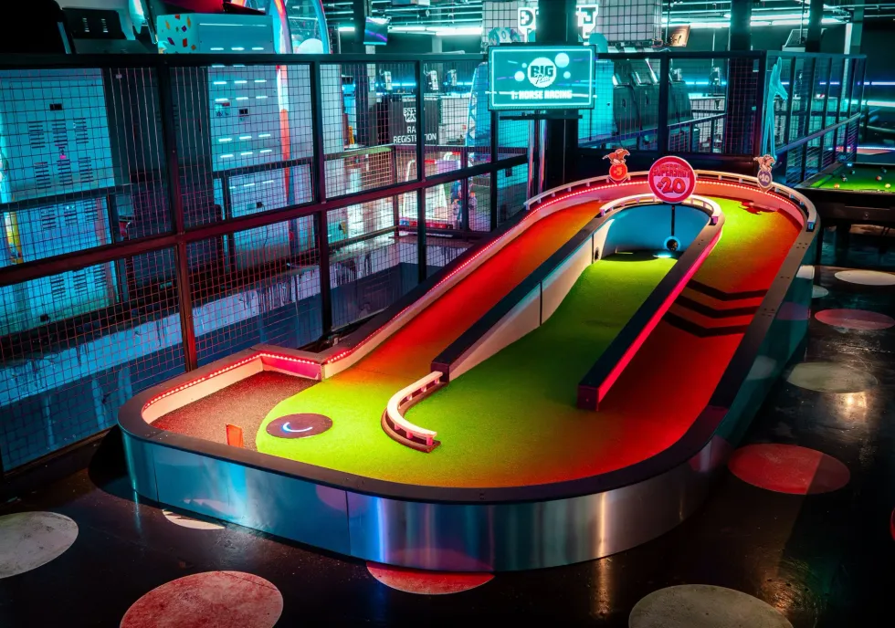 Mini-golf course with neon lights and vibrant colors in an indoor arcade setting.