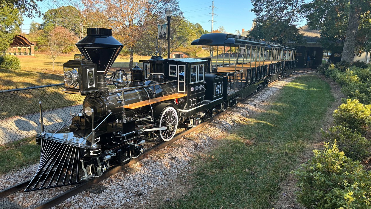 Miniature black locomotive engine on tracks in a park setting.