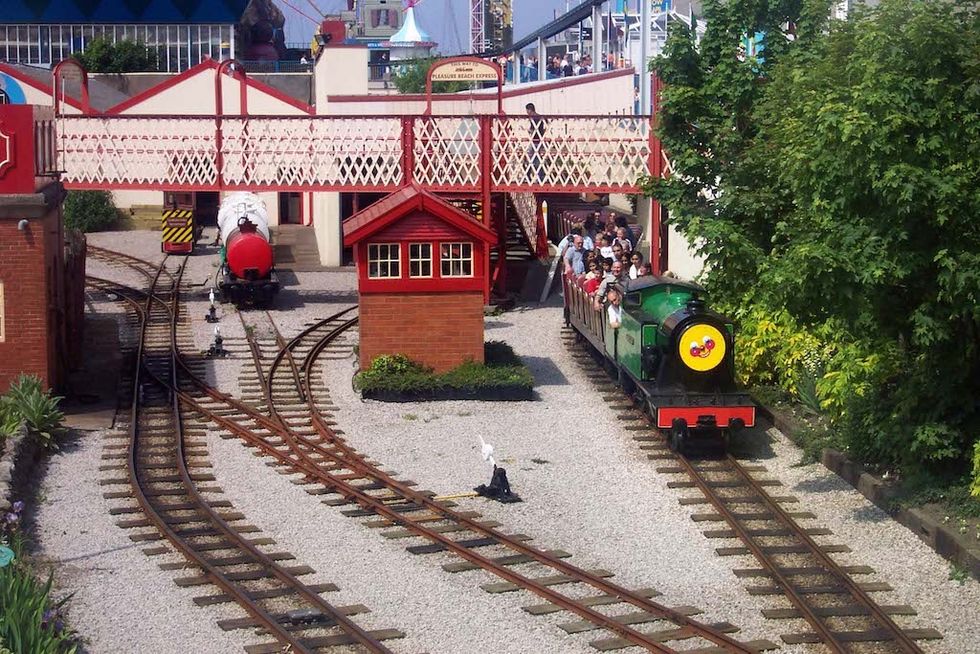 Miniature railway with a green train and passengers under a decorative footbridge.