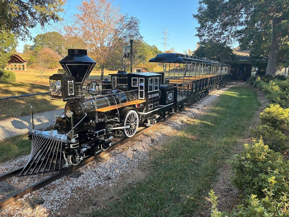 Miniature train on a track in a park setting with trees and grass.