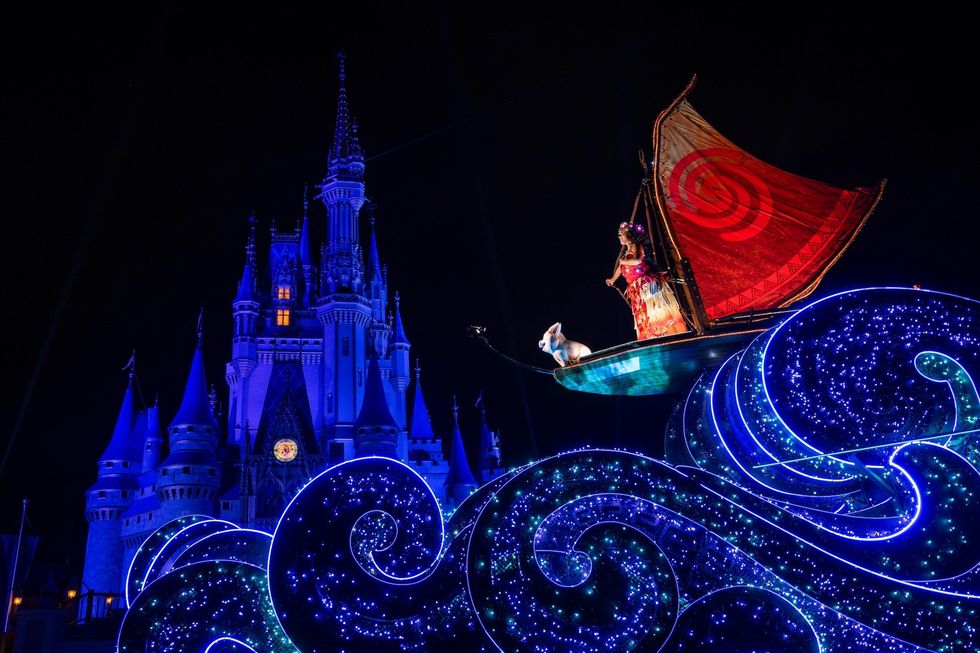 Moana on illuminated float with waves and castle in background at night.