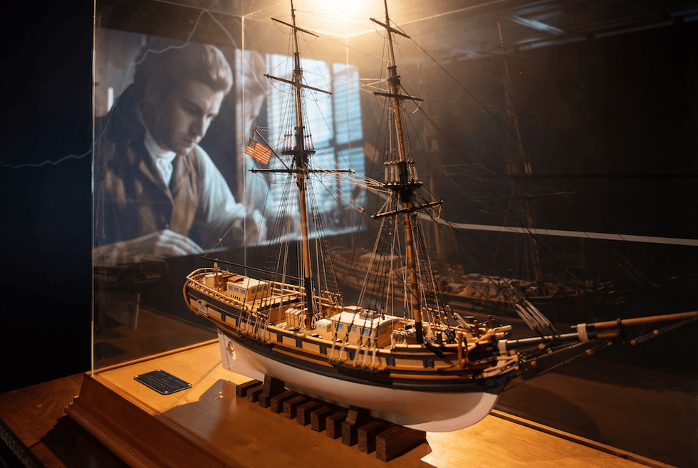 Model ship on display with a historical figure in the background, The First Salute exhibition