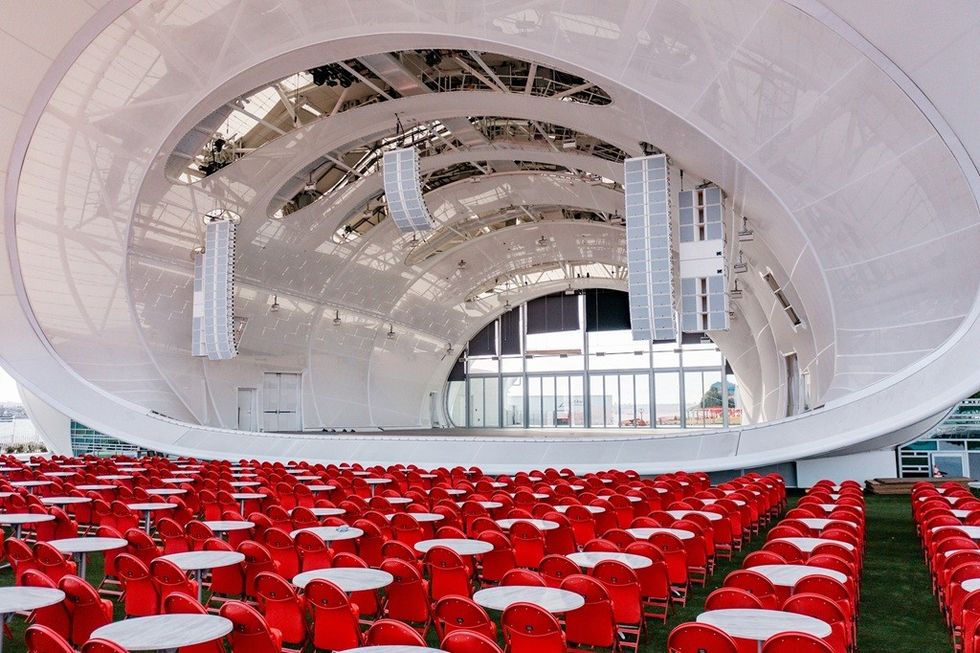 Modern amphitheater with red chairs, white tables, and large overhead speakers.