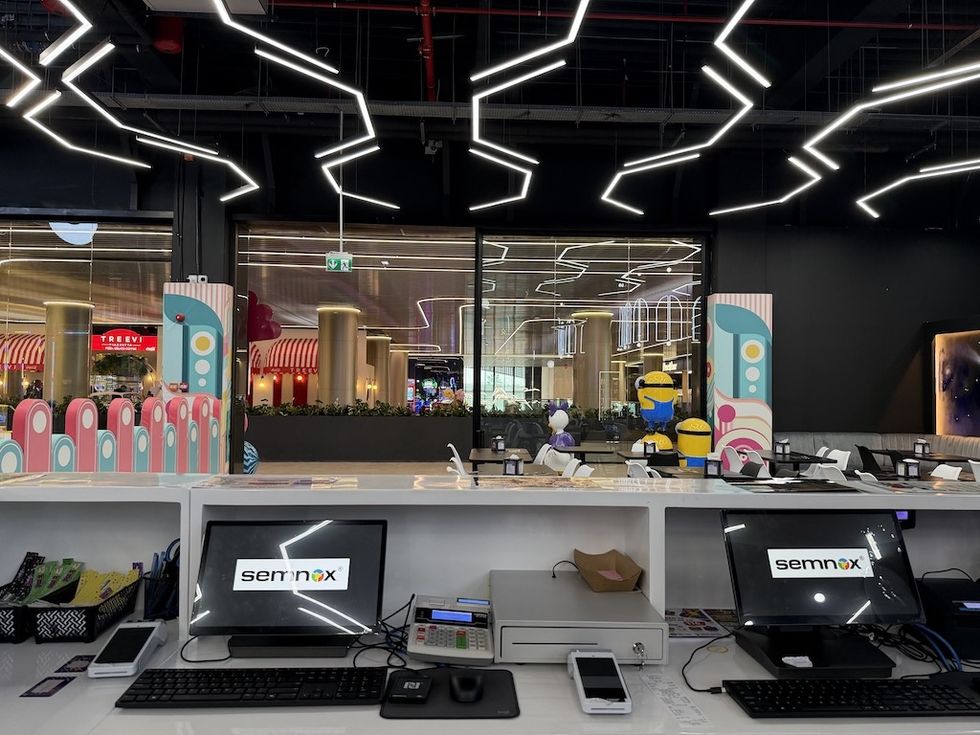 Modern arcade counter at Funzy Playground with computers showing Semnox logo, vibrant decor, and futuristic ceiling lighting.