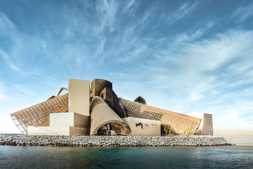 Modern architectural building called Guggenheim Abu Dhabi with geometric shapes against a blue sky, near water.