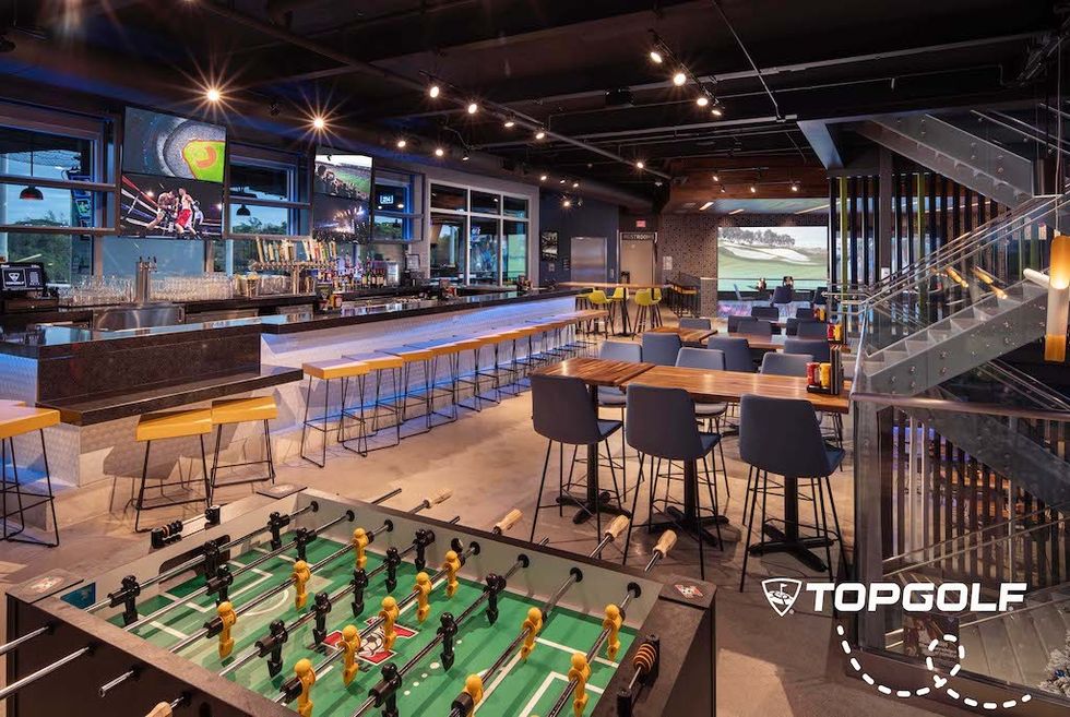 Modern bar with foosball, large screens, and seating at Topgolf venue.