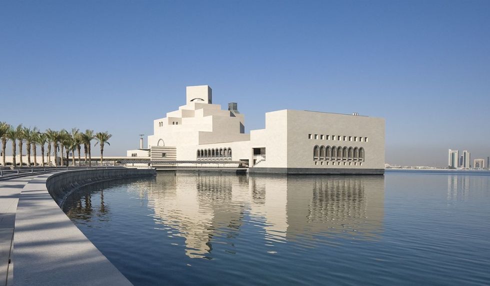 Modern beige building named the Museum of Islamic Art, reflected in water under a clear blue sky.