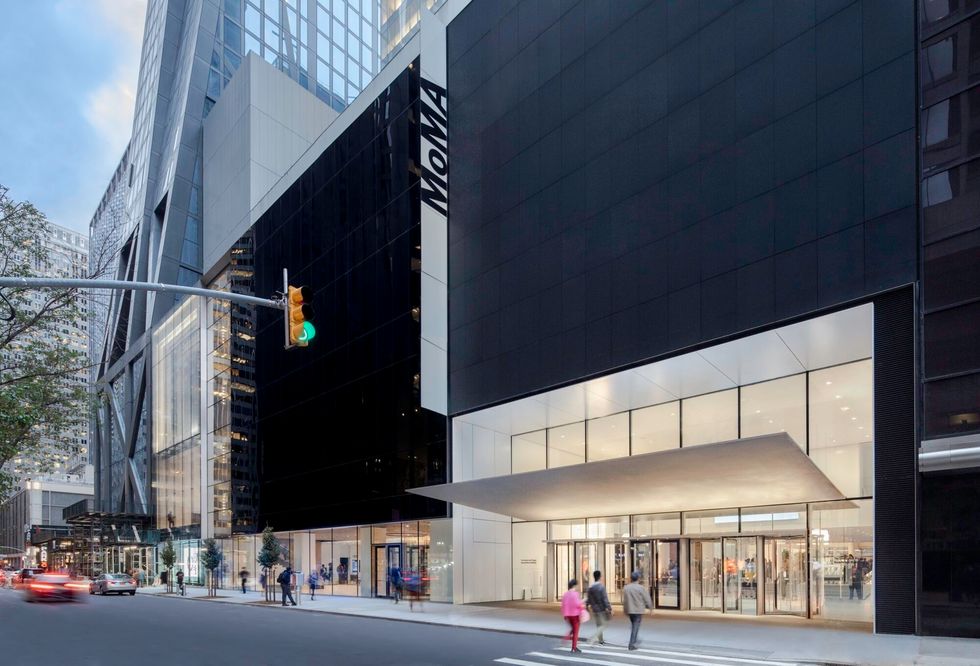 Modern black-and-glass MoMA building with a brightly lit street-level entrance and pedestrians.