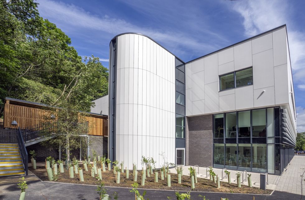 Modern building called The Light with curved and angular facades, surrounded by greenery and blue sky.
