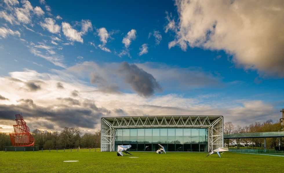 Modern building called the Sainsbury Centre in Norwich with glass walls and red sculpture, set against a cloudy blue sky
