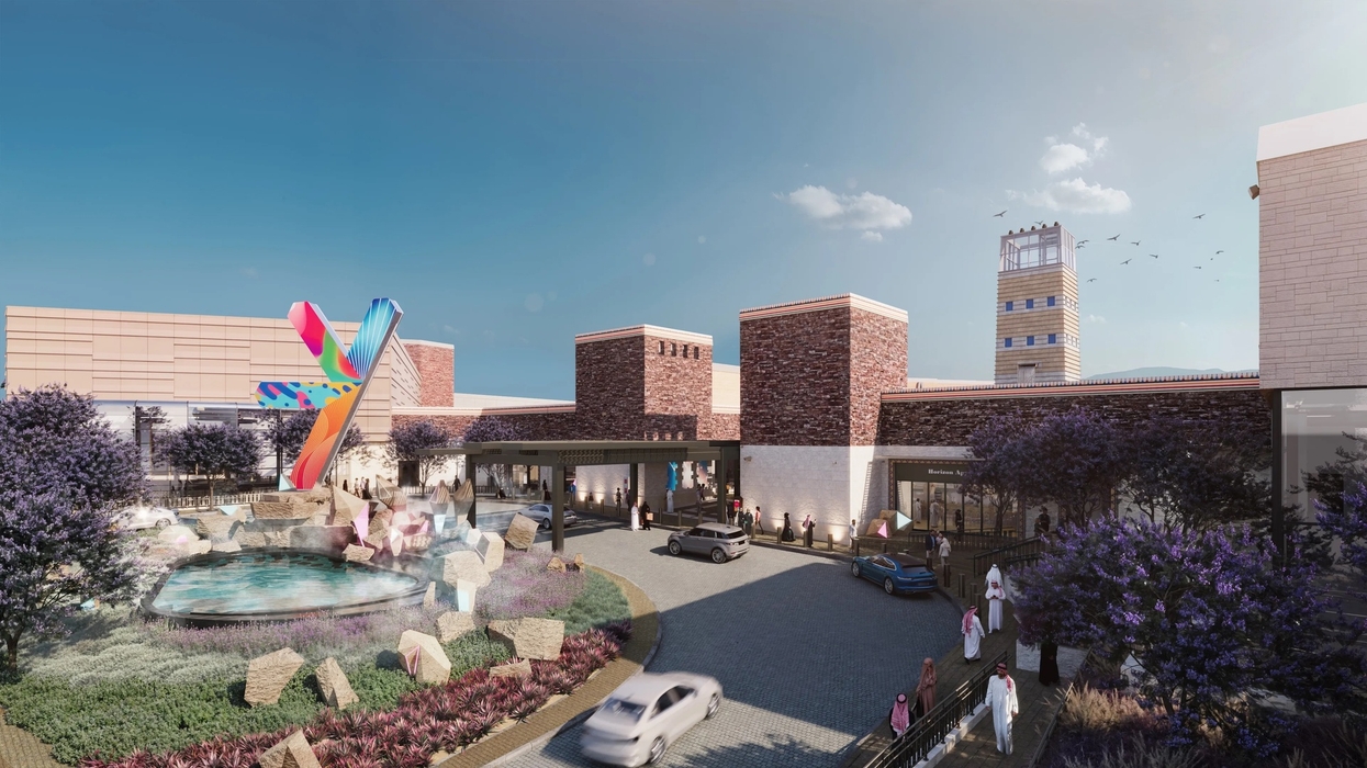 Modern building exterior with colorful sculpture, fountain, cars, and people under a clear sky in Abha, Saudi Arabia