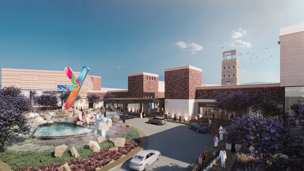 Modern building exterior with colorful sculpture, fountain, cars, and people under a clear sky in Abha, Saudi Arabia