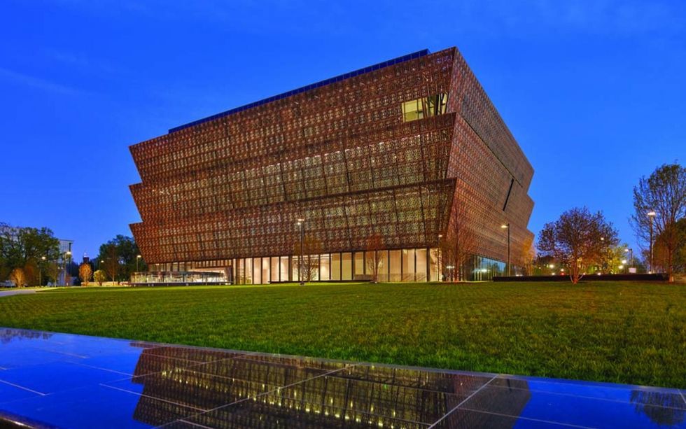 Modern building, National Museum of African American History and Culture, with a layered design, surrounded by grass, under a twilight sky.