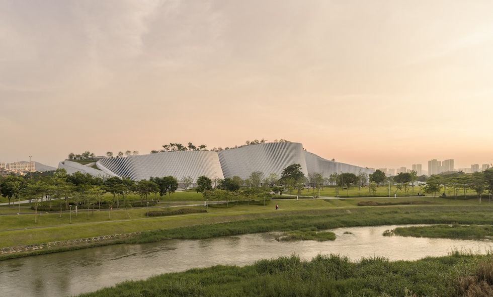 Modern building, Shenzhen Natural History Museum, with rooftop greenery, surrounded by a park and river at sunset.