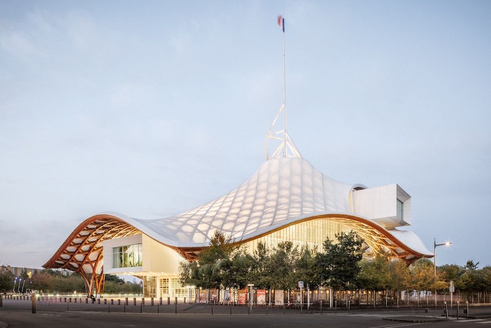 Modern building, the Centre Pompidou-Metz, with a wavy, tent-like roof and trees in front, under a clear sky.