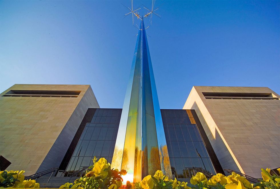 Modern building, the National Air and Space Museum, with a tall, reflective blue spire against a clear sky, surrounded by yellow flowers.