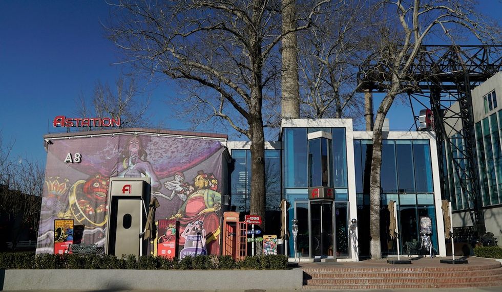 Modern building with colorful murals, large glass windows, and statues, surrounded by trees.